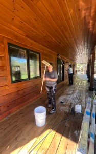 Two people staining a wooden porch ceiling and floor