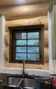 Rustic kitchen window with log frame, double sink, and stone countertop