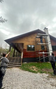 Workers renovating a rustic cabin exterior with scaffolding on a cloudy day