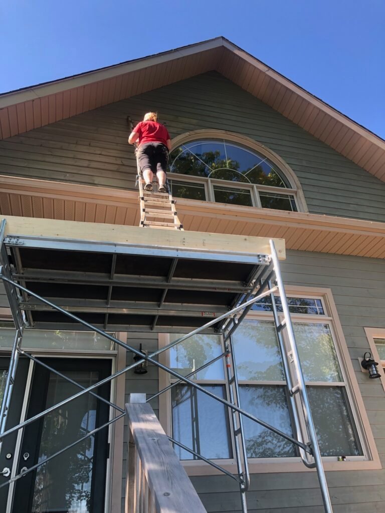 Person painting exterior of a two-storey house on a ladder