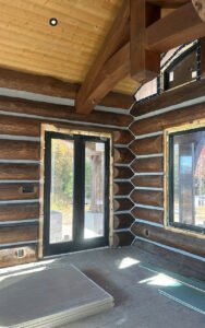 Interior of a log cabin under construction, showcasing log walls and large windows
