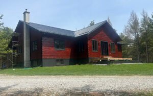 Red wooden house with black roof amidst trees, recent construction