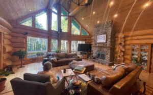 Spacious log cabin living room with stone fireplace, leather couches, large windows