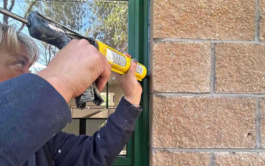 Person caulking window frame for professional maintenance service