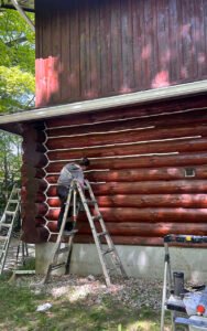 Person painting a red log cabin exterior with white trim