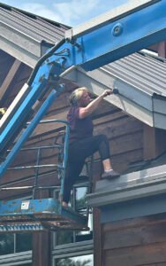Worker on lift repairing building exterior with blue sky backdrop