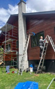 Person painting exterior of house with ladder and scaffolding