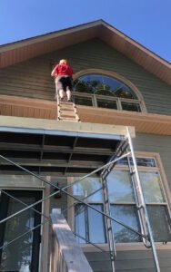 Worker on a scaffold painting a two-story house exterior