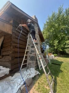 Workers restore log cabin using ladders and tools