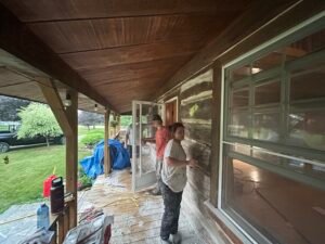 People restoring the exterior of a wooden house on a porch