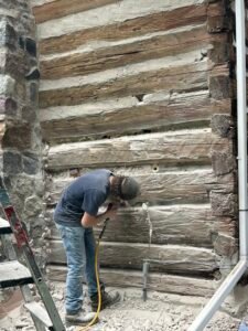 Log cabin restoration with worker using pneumatic drill