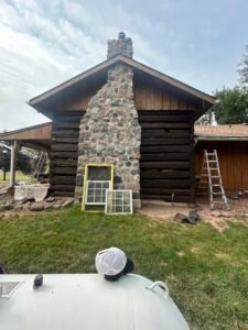 Rustic log cabin restoration with stone chimney and tools