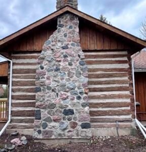 Stone chimney of historic log cabin under cloudy sky