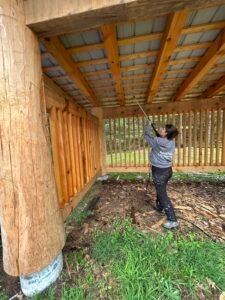 Person pressure washing wooden pavilion structure with logs