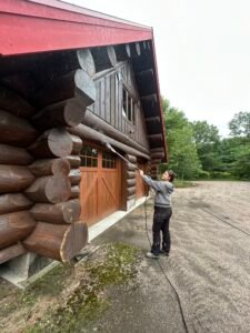 Woman pressure washing a log cabin with a red roof