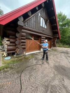 Person power washing log cabin exterior with wooden doors